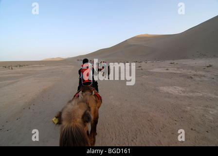 Camel caravan con i turisti di fronte le dune di sabbia del deserto del Gobi e il Monte Mingshan a Dunhuang, Silk Road, del Gansu Chi Foto Stock