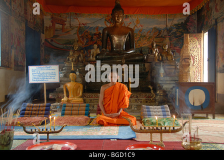 Il Buddismo Theravada, un monaco in un tempio, antica statua del Buddha in bronzo, meditazione, bhumisparsha mudra gesto di chiamando Foto Stock