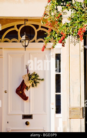 Tradizionale casa Regency con ricamate Calza di Natale con holly appeso sulla porta. Un inglese Cotswold Town House. Foto Stock