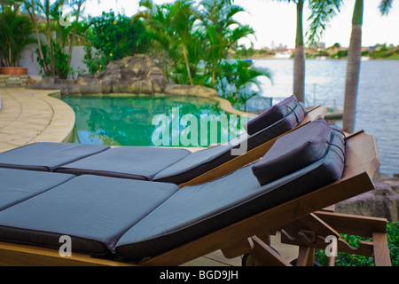 Sedie a sdraio a bordo piscina tropicale a waterfront mansion Foto Stock