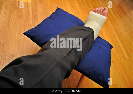 Dettaglio di un uomo si è rotto una gamba in un calco in gesso, in appoggio su di un cuscino Foto Stock