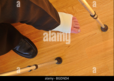 Dettaglio di un uomo si è rotto una gamba in un calco in gesso, con le stampelle Foto Stock