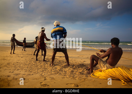 I pescatori in Kovalam Kerala nel primo mattino alaggio nelle reti da pesca da barche da pesca che uscì a notte Foto Stock