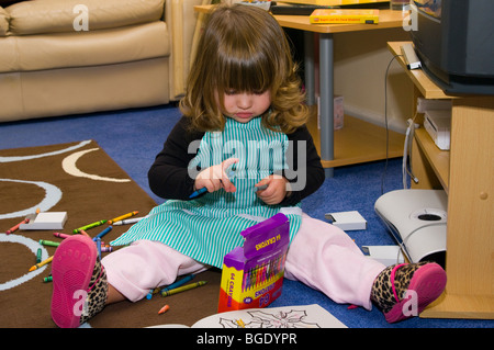 Ragazza giovane seduto sul pavimento con le matite di colorazione e libro da colorare Foto Stock