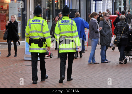 Agenti di polizia indietro vista due di un genere di poliziotti a piedi pattuglia camminare lungo la strada commerciale affollata in città di Chelmsford Essex Inghilterra Regno Unito Foto Stock