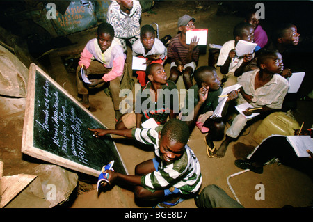 Homeless Street i bambini frequentano una scuola serale gestito da una carità locale dove vivono in oggetto di dumping automobili, Luanda Foto Stock