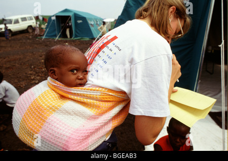 Mugungo Camp, regione di Goma, Zaire, luglio 1994. Un aiuto lavoratore svolge un orfano bambino sulla schiena. Foto Stock