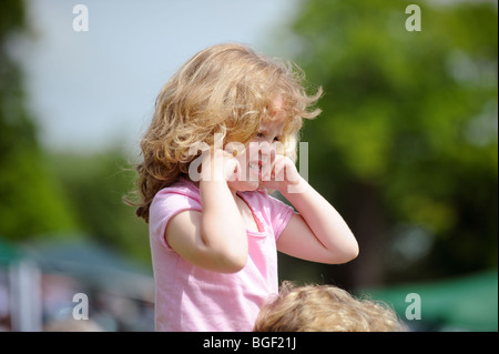 Una giovane ragazza mette le sue dita nelle sue orecchie per attutire la musica ad alto volume a un evento estivo nel Sussex. Foto Stock