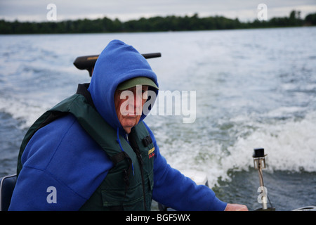 Senior anziani condito guida di pesca la guida alumnacraft barca da pesca nel freddo umido meteo instabile acqua onde wake azione Foto Stock