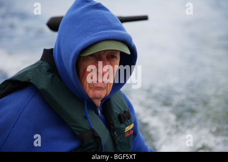 Senior anziani condito guida di pesca la guida alumnacraft barca da pesca nel freddo umido meteo instabile acqua onde wake azione Foto Stock