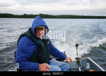 Senior anziani condito guida di pesca la guida alumnacraft barca da pesca nel freddo umido meteo instabile acqua onde wake azione Foto Stock