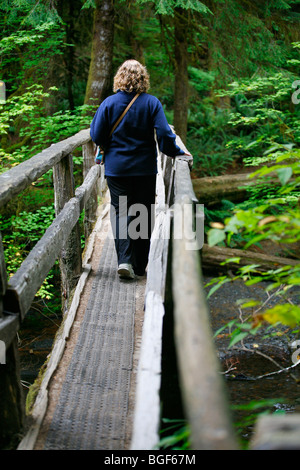 Donna che cammina su un ponte sul sentiero per Marymere Falls, sulla Penisola Olimpica, il Parco Nazionale di Olympic, nello Stato di Washington. Foto Stock