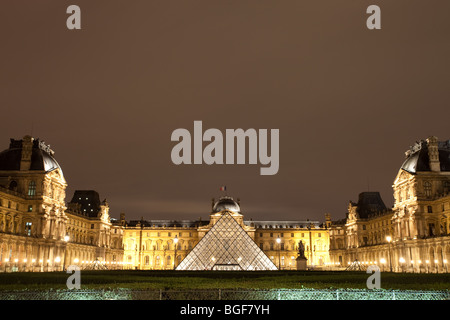 Il museo del Louvre e la piramide triangolare illuminata di notte dalla giostra Foto Stock