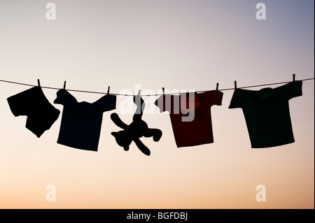 Abbigliamento per bambini e orso di peluche su una linea di lavaggio silhouette al tramonto. India Foto Stock