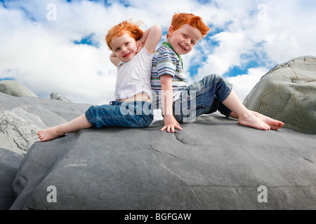 Un bambino di cinque anni, un ragazzo e una bambina di tre anni sit back to back su rocce alla costa gallese. Foto Stock