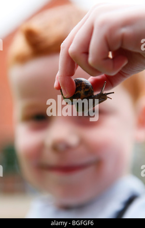 Un bambino di cinque anni, ragazzo giocando con una lumaca nel suo giardino Foto Stock