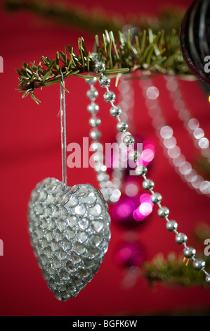 Un colorato a forma di cuore decorazione ninnolo splendidamente collocato su un pino albero di Natale su uno sfondo di colore rosso. Foto Stock
