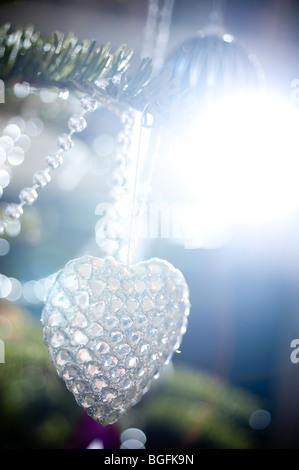 Un colorato a forma di cuore decorazioni ninnolo splendidamente collocato su un pino albero di Natale in un salotto. Foto Stock