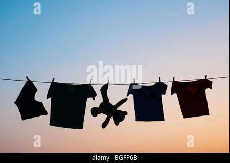 Abbigliamento per bambini e orso di peluche su una linea di lavaggio silhouette all'alba. India Foto Stock