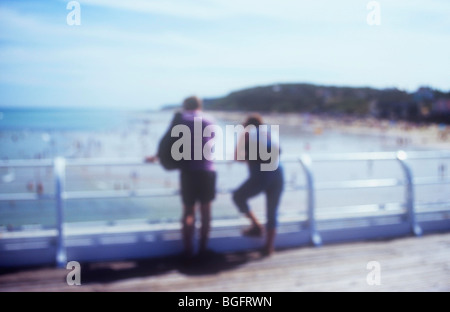 Impressionistica vista del giovane appoggiata sulle ringhiere del molo e guardando fuori attraverso il mare e la spiaggia verso le scogliere Foto Stock