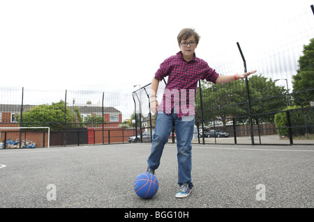 Ragazzo controllato in maglietta e jeans giocando con sfera blu in ambiente urbano il campo di calcio Foto Stock