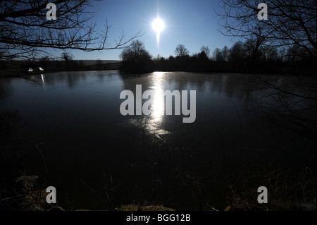Sun glinting sul laghetto congelato a Falmer village vicino a Brighton SUSSEX REGNO UNITO Foto Stock