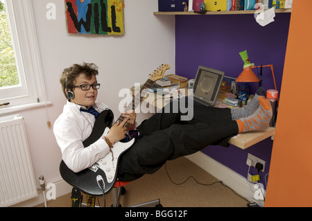 Ragazzo seduto sulla sedia in camera da letto a suonare la chitarra con i piedi Foto Stock