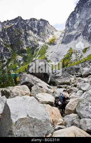 Una donna escursionismo attraverso un campo di Boulder vicino Colchuck lago sottostante Aasgard passano in cascate montagne dello Stato di Washington, USA. Foto Stock
