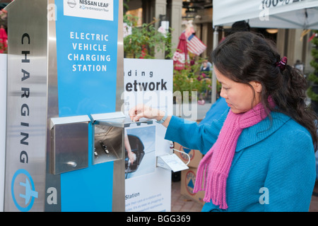 Donna che guarda al display promozionali sul veicolo elettrico delle stazioni di caricamento delle infrastrutture di rete. Foto Stock