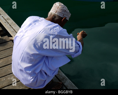 Omani uomo in abito tradizionale la pesca da un molo vicino al Moscato mercato del pesce Foto Stock