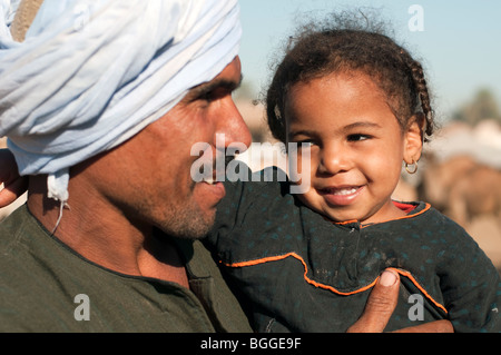 Giovane padre egiziano con sua figlia in pig-tail in un mercato di cammelli lungo il Nilo. Foto Stock