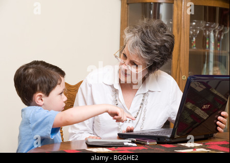 Active senior donna paga le bollette di casa online con l aiuto della nipote usando un computer portatile. Foto Stock