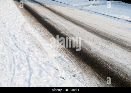 Tracce di pneumatici su vuota una strada coperta di neve e ghiaccio Foto Stock