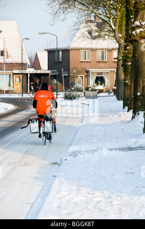 Un postino olandese in bicicletta lungo una strada innevata nei Paesi Bassi Foto Stock