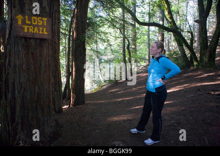 Una donna escursionismo su un sentiero si ferma per leggere un cartello che dice "perso Trail" in corrispondenza di una spaccatura nel percorso, Muir Woods monumento nazionale Foto Stock