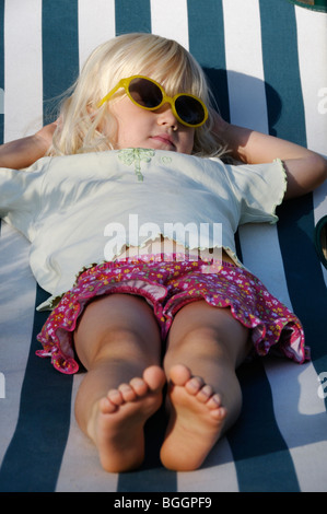 Stock Foto di un bambino di 4 anni ragazza distesa su un lettino solare con occhiali da sole. Foto Stock