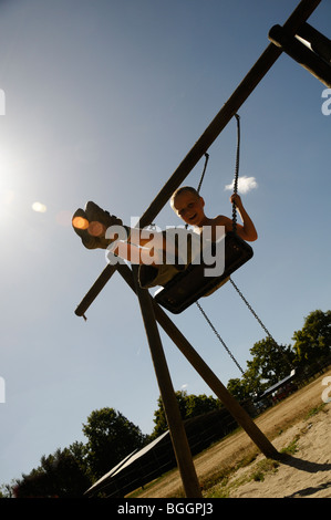 Foto di stock di un 8 anno vecchio ragazzo basculante in altalene nel parco giochi. Foto Stock