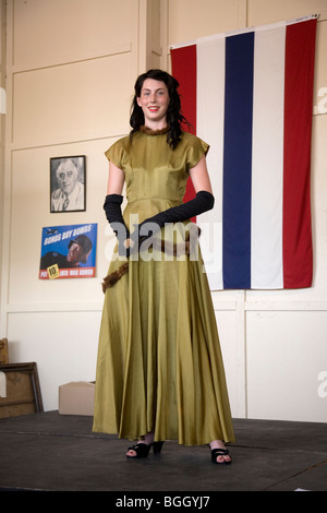 Donna attraente negli anni quaranta capi di abbigliamento in posa davanti alla bandiera durante una rievocazione storica di una guerra mondiale II sfilata di moda Foto Stock