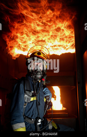 Un vigile del fuoco in un edificio con le fiamme dietro di lui e a soffitto Foto Stock