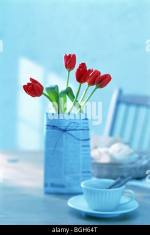 Tulipani rossi avvolti in un giornale su un tavolo per la colazione Foto Stock