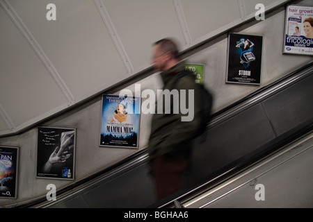 Un uomo su una scala mobile che passa la pubblicità sulla metropolitana di Londra Centrale, UK. Foto Stock