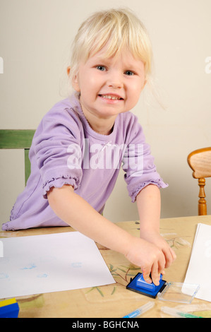 Foto di stock di un 4 anno vecchia ragazza utilizzando inchiostro timbri durante un gioco creativo sessione. Foto Stock
