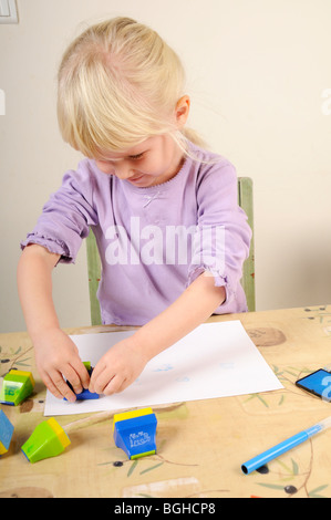 Foto di stock di un 4 anno vecchia ragazza utilizzando inchiostro timbri durante un gioco creativo sessione. Foto Stock