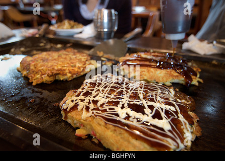 Okonomi yaki. Stile giapponese gustosi pancake cotti su una piastra calda. Giappone Foto Stock