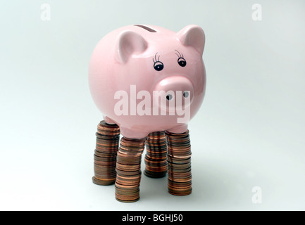 Salvadanaio,PIGGYBANKS piedi su pile di monete Britanniche re l'economia dei redditi del risparmio ipoteche l'economia UK Foto Stock