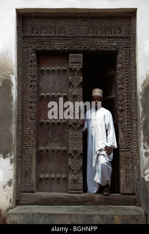 Stone Town, Zanzibar, Tanzania. Un africano Zanzibari indossando il tradizionale Kanzu e Kofia (HAT) sorge nel vano della porta. Foto Stock