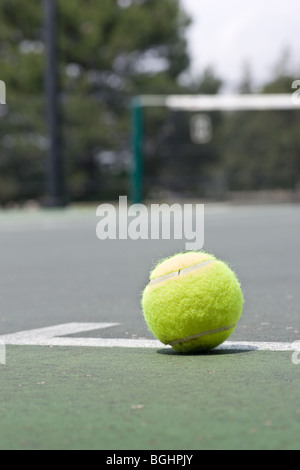 Un primo piano di un giallo palla da tennis appena al di fuori della linea di base su un asfalto campo da tennis, con un netto sfocata in background Foto Stock