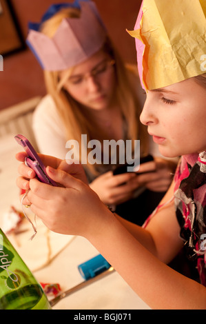 Due giovani sorelle adolescenti ragazze carta da indossare cappelli partito texting sui loro telefoni cellulari dopo il giorno di Natale la cena, REGNO UNITO Foto Stock