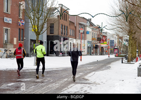Tre corridori rendendo il loro modo attraverso la snowy principale strada dello shopping nella città olandese di Veenendaal Foto Stock