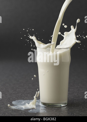 Versare il latte in vetro su uno sfondo grigio Foto Stock